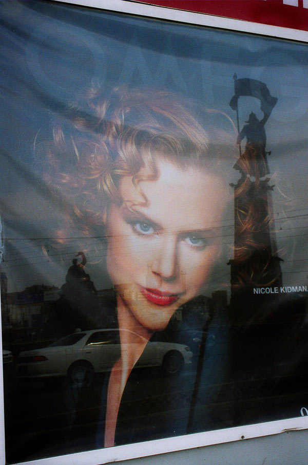 Плакат с изображением Николь Кидман в витрине и там же - отражение главного памятника на центральной площади во Владивостоке.