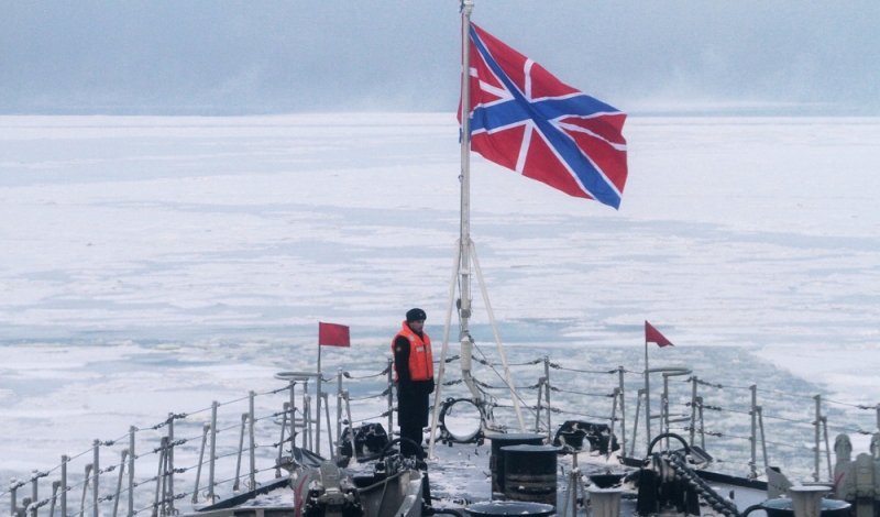 Матрос Северного флота стоит на посту у военно-морского флага на военном корабле.
